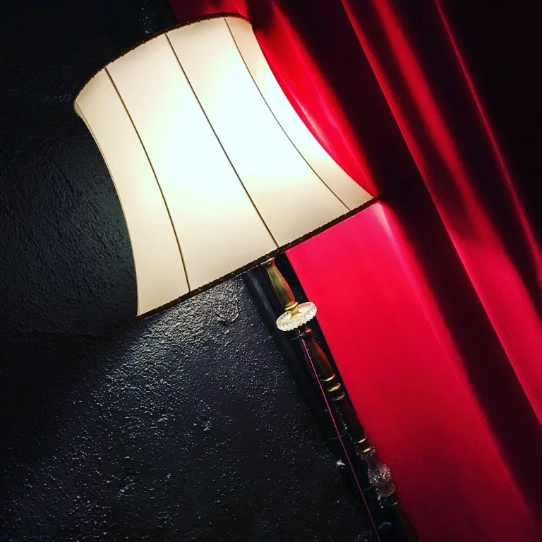 Stehleuchte mit hellem Stoffschirm vor rotem Samtvorhang und dunkler Wand