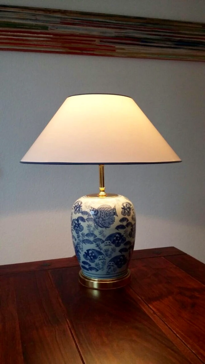 Tischlampe mit blau-weißem Keramikfuß und beigem Schirm auf Holztisch
