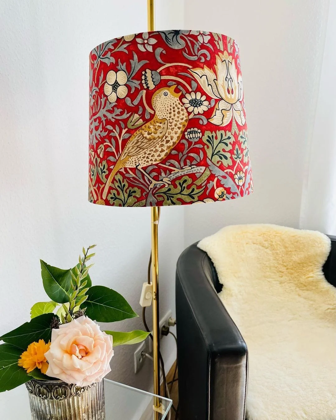 Roter Lampenschirm mit Vogel- und Blumenmuster an goldener Stehlampe neben Sessel
