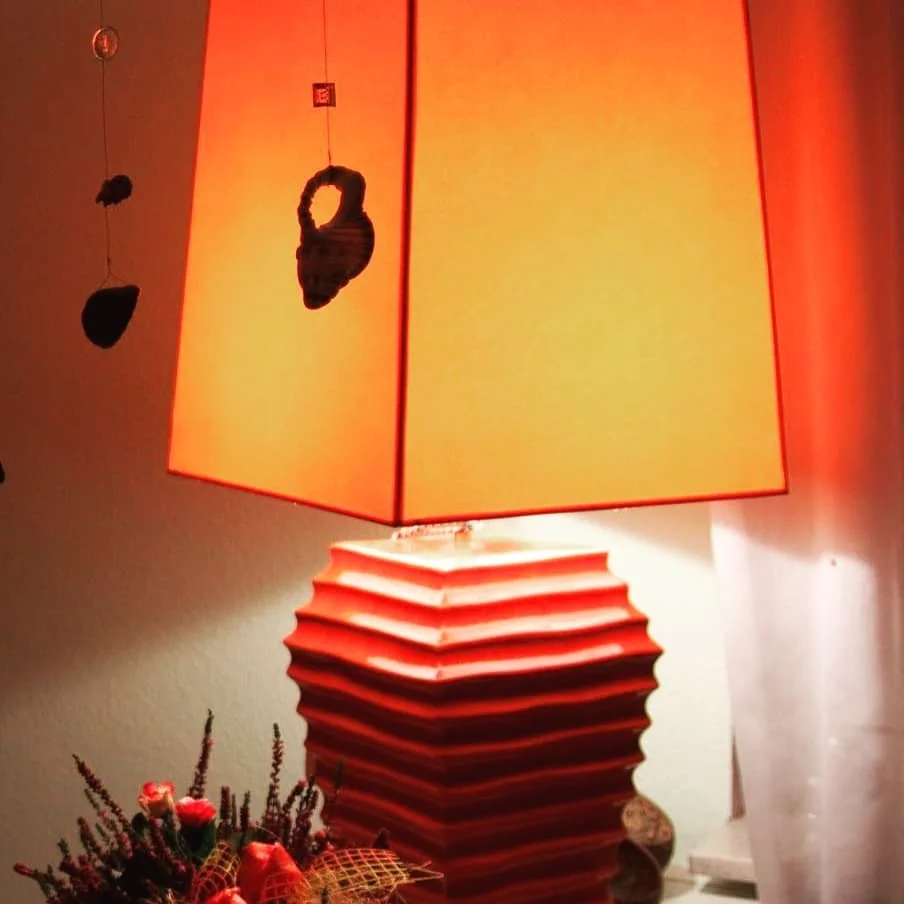 Tischlampe mit orangefarbenem rechteckigen Schirm und gestuftem Sockel, Blumenarrangement daneben
