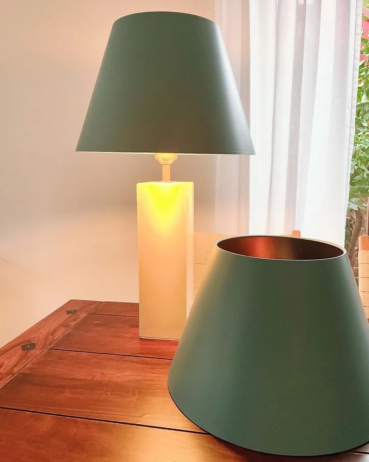 Grüne Lampenschirme, einer auf einem beleuchteten Lampenfuß, einer liegend auf einem Holztisch