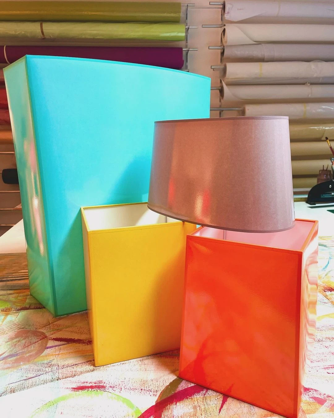 Bunte kastenförmige Lampenschirme und ein zylindrischer Lampenschirm auf Stoffunterlage