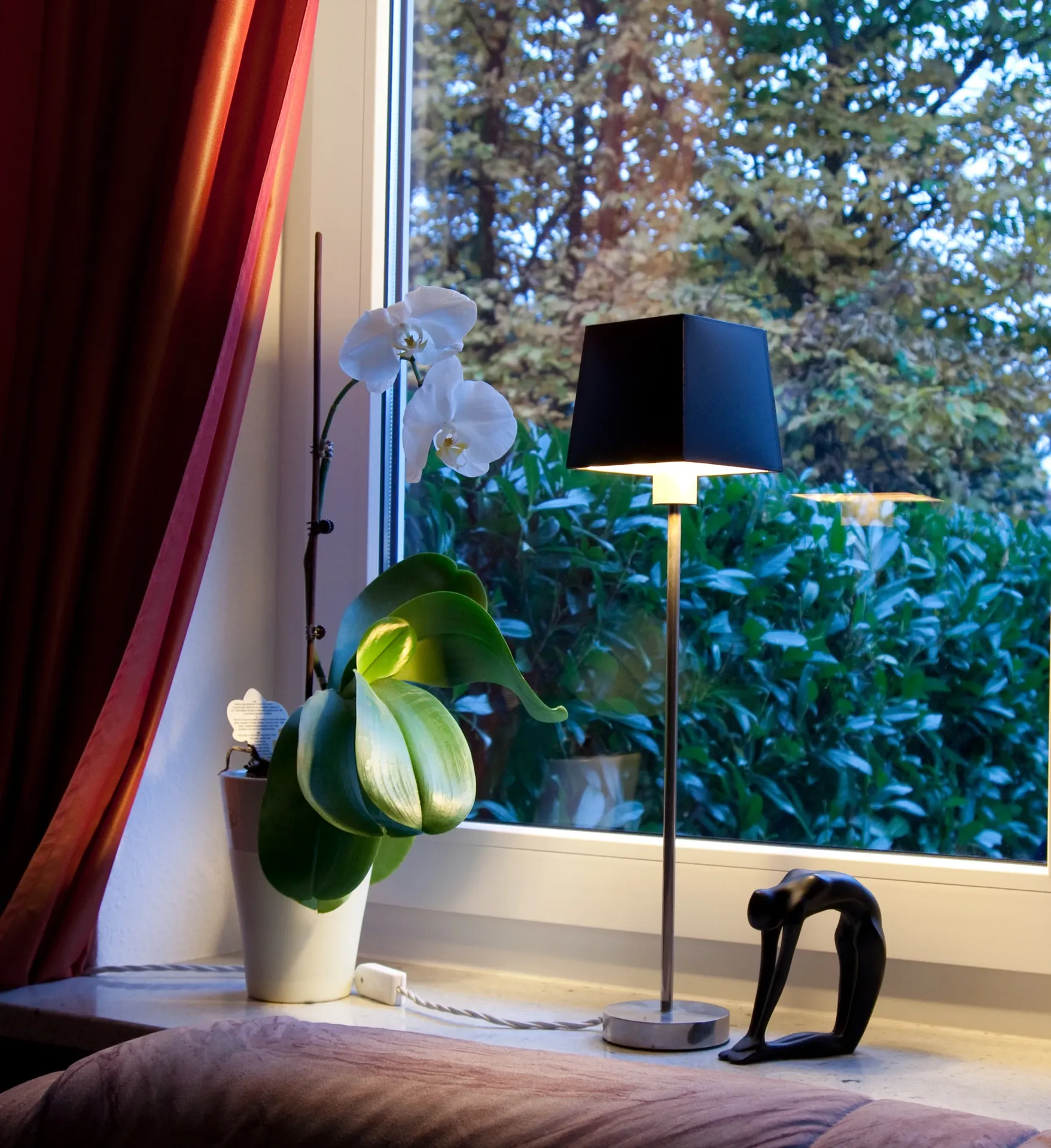 Tischlampe mit schwarzem Schirm auf Fensterbank neben weißer Orchidee