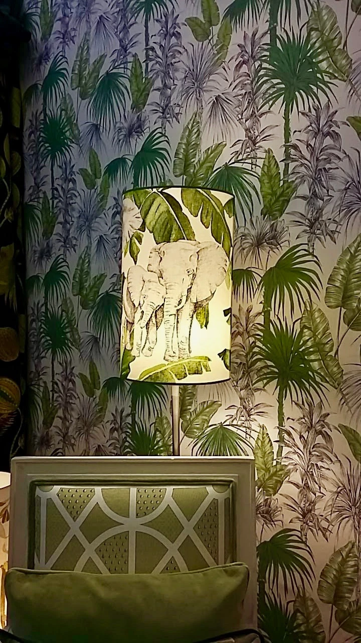 Lampe mit Elefantenmotiv auf Lampenschirm vor tropisch gemusterter Tapete
