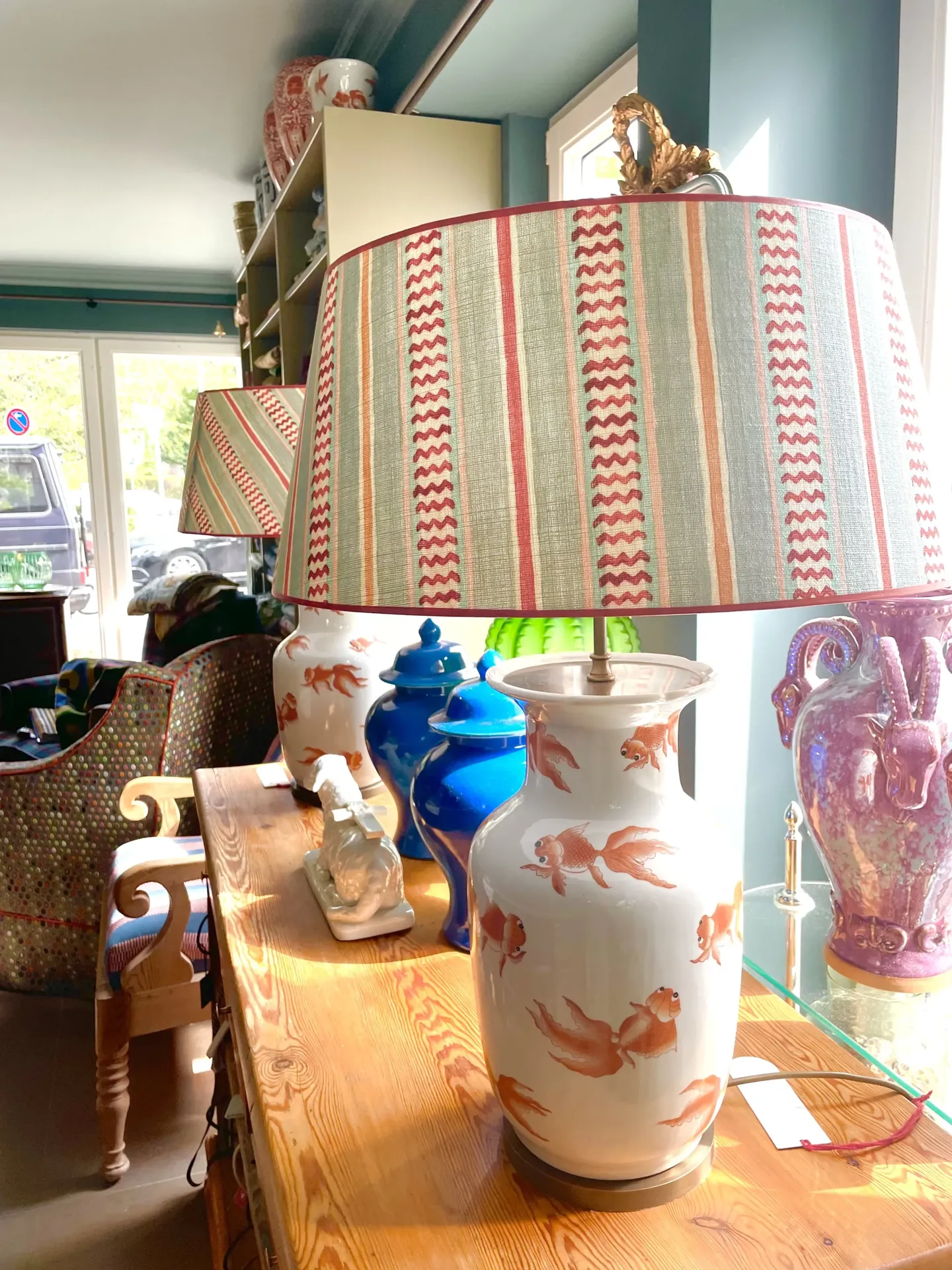 Tischlampe mit gestreiftem Schirm und Keramikfuß mit Goldfischmotiven auf Holztisch im Laden