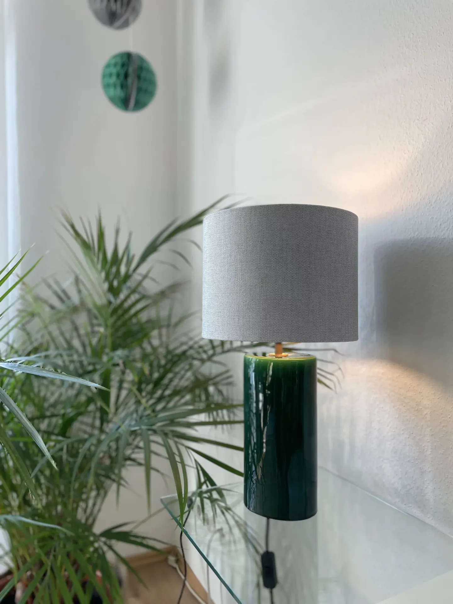Tischlampe mit grünem Keramikfuß und hellem Leinenschirm neben Zimmerpflanzen