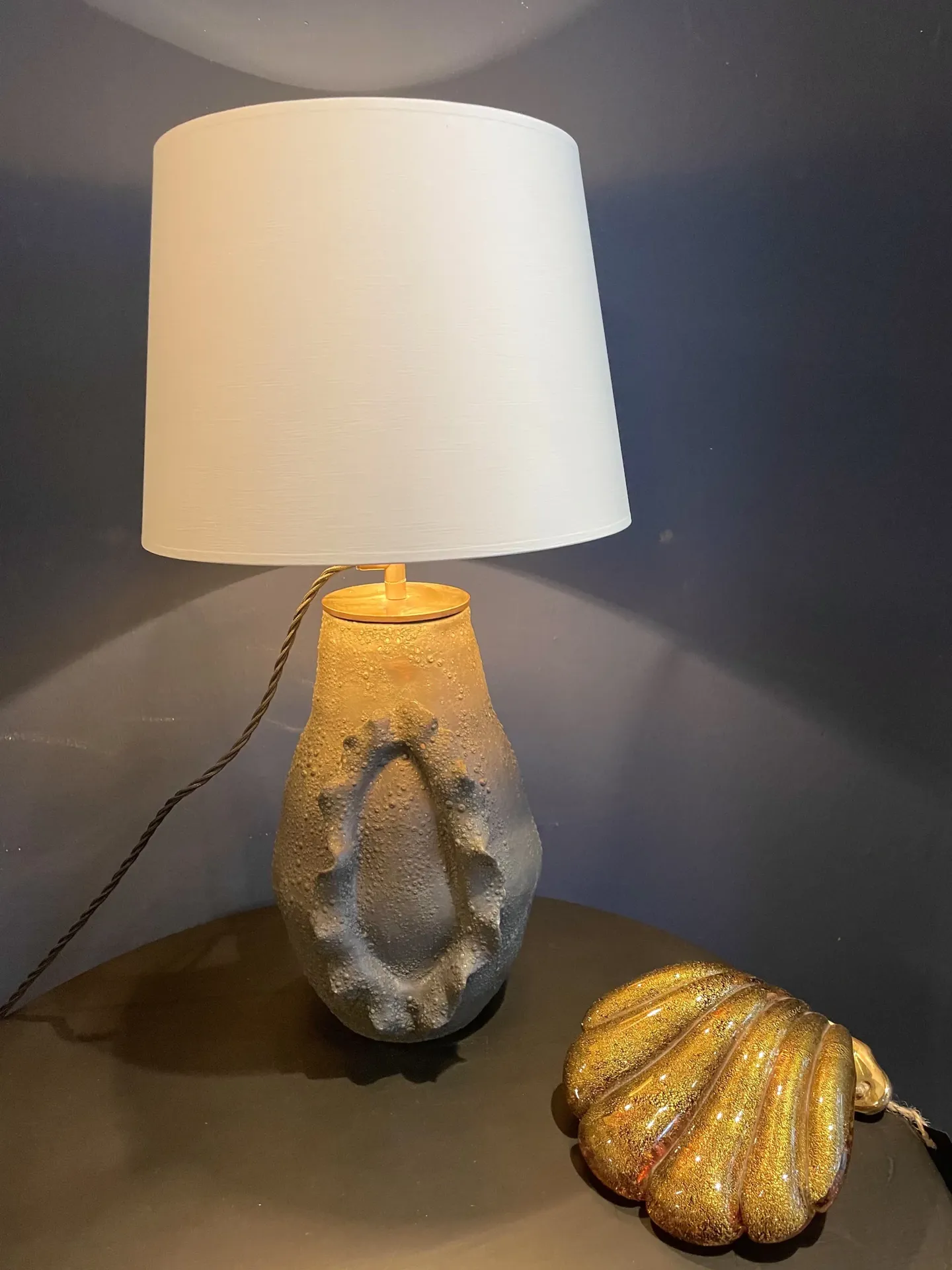 Keramik-Tischlampe mit weißem Lampenschirm neben goldener Dekomuschel
