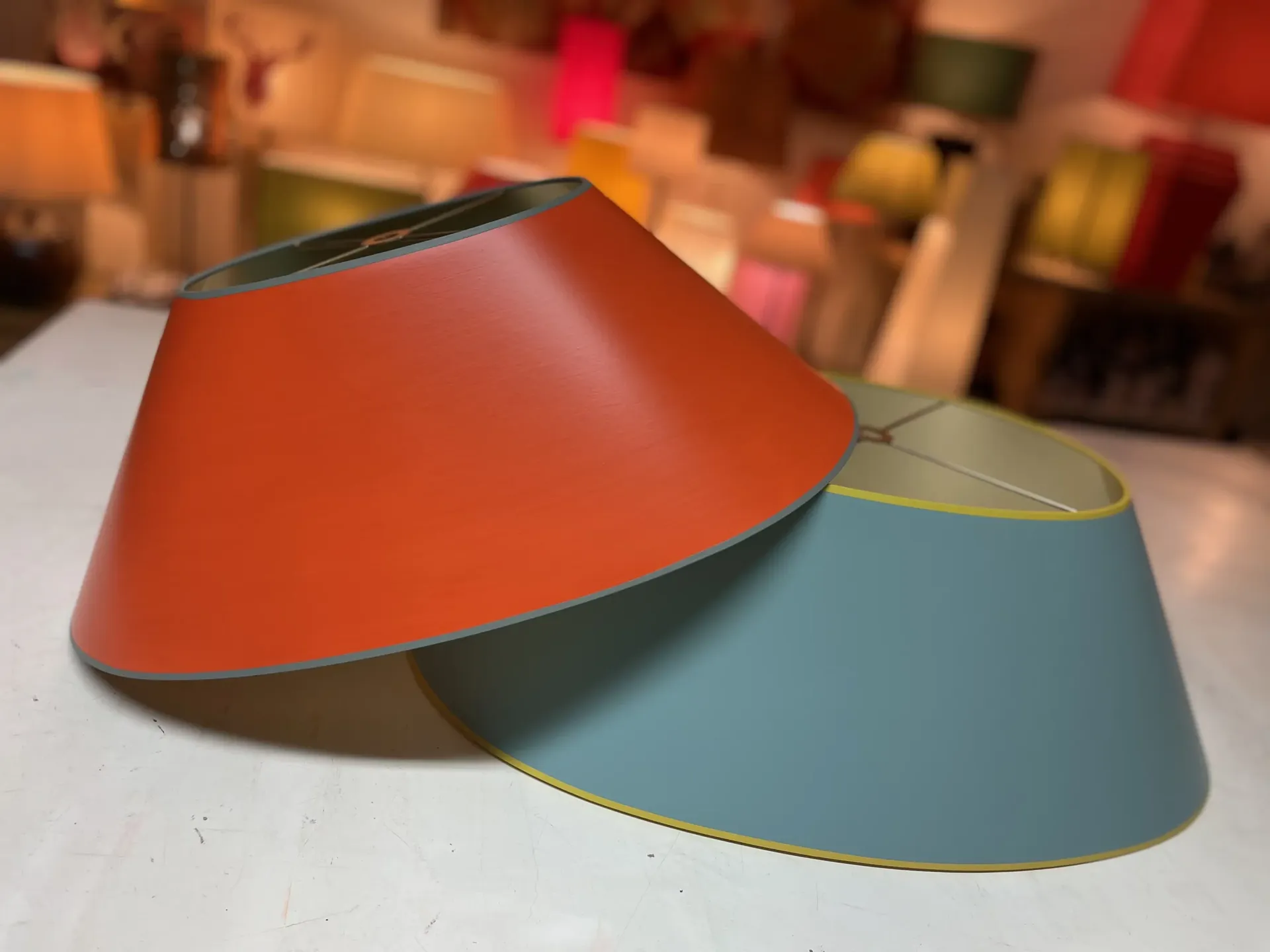 Zwei konische Lampenschirme, überlappend auf einem Tisch mit Lampen im Hintergrund