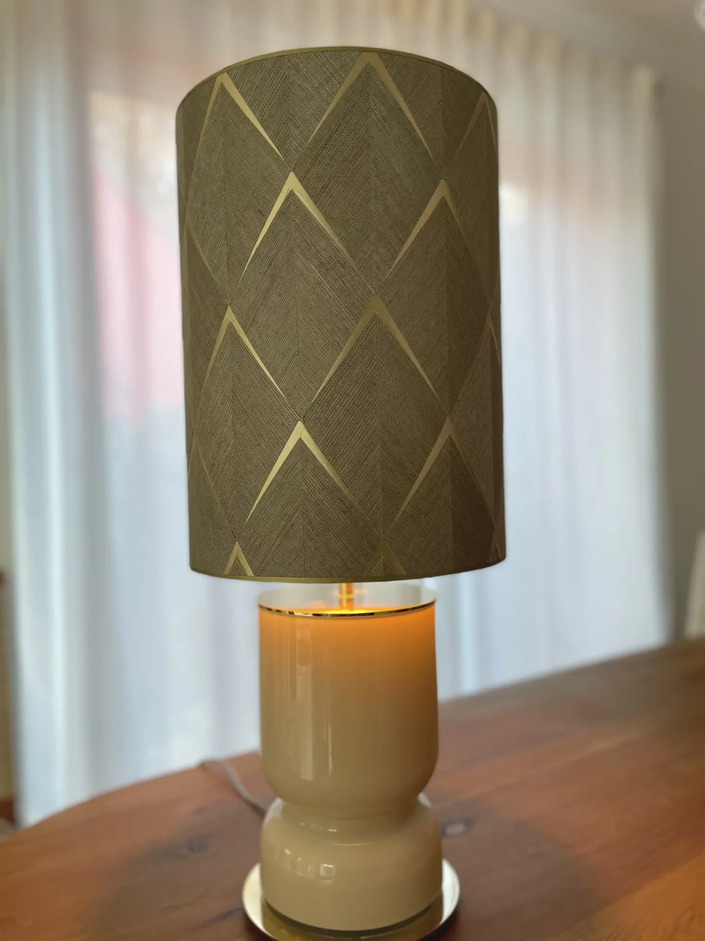 Tischlampe mit zylindrischem, grafisch gemustertem Lampenschirm und cremefarbenem Keramikfuß