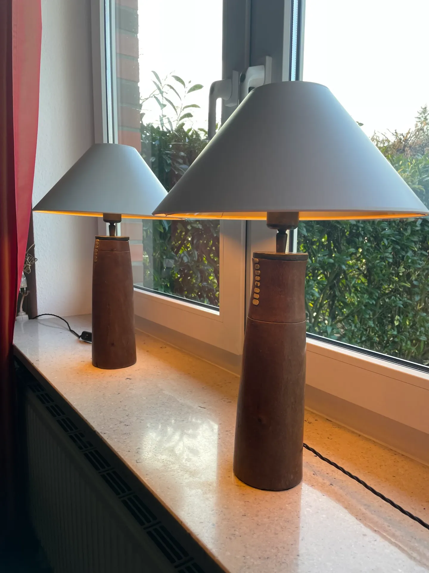 Zwei Tischlampen mit grauen Schirmen und Holzsockeln auf der Fensterbank