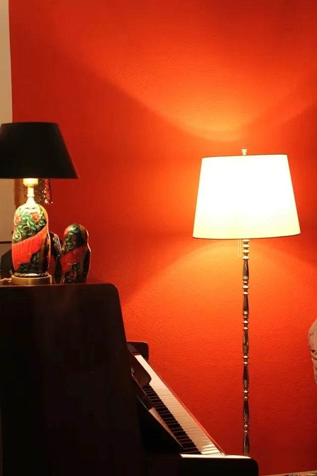 Steh- und Tischlampe neben einem Klavier vor roter Wand