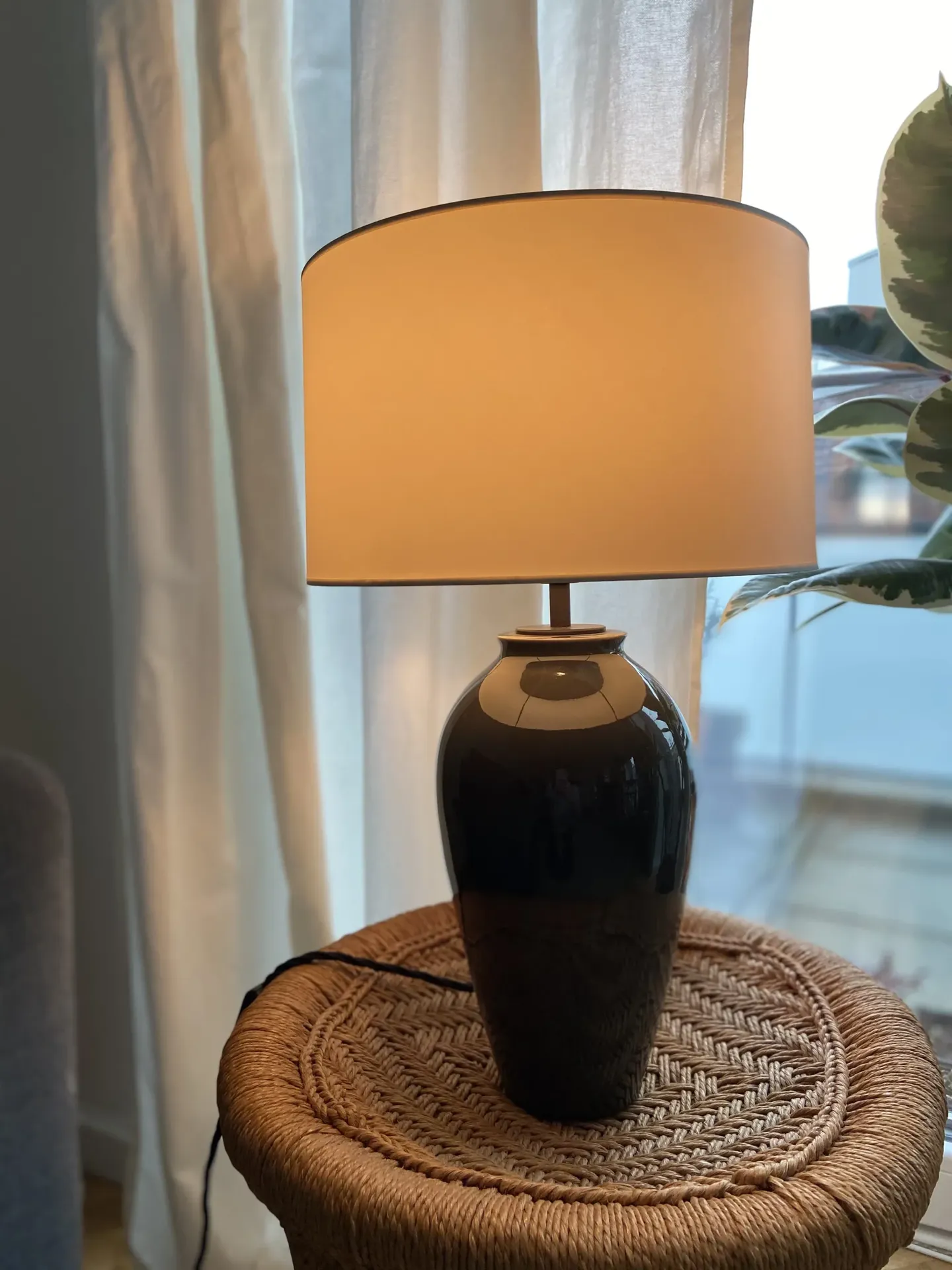 Keramische Tischlampe mit hellem Stoffschirm auf geflochtenem Hocker