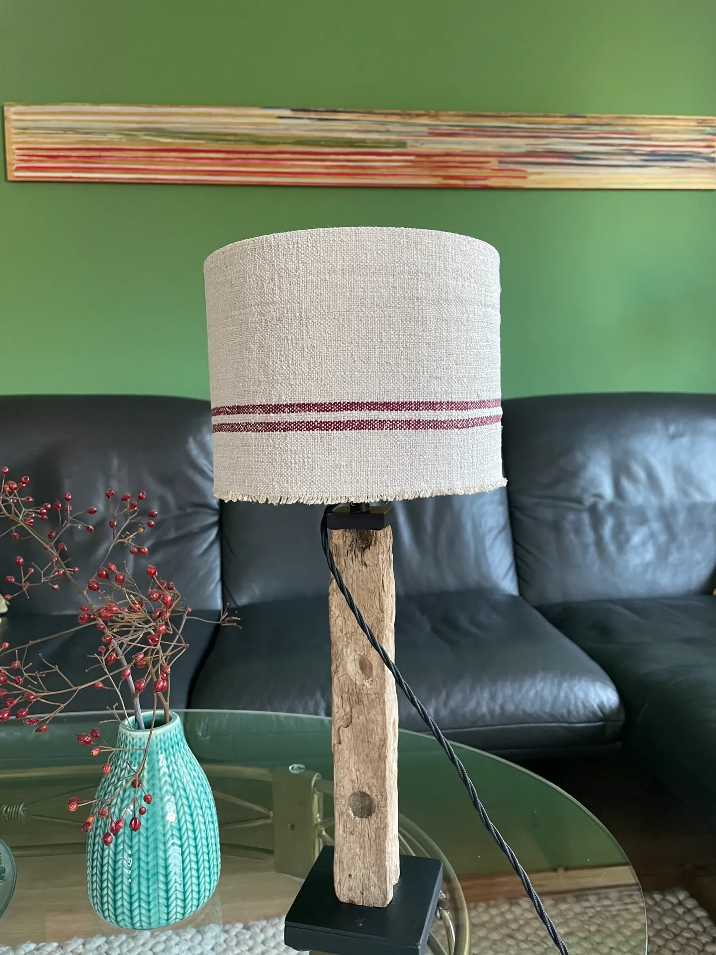 Tischlampe mit Leinenlampenschirm und rustikalem Holzfuß vor grünem Sofa
