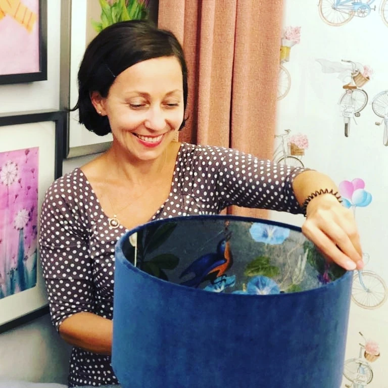 Eine Frau lächelt und hält einen blauen Lampenschirm mit gemusterter Innenseite