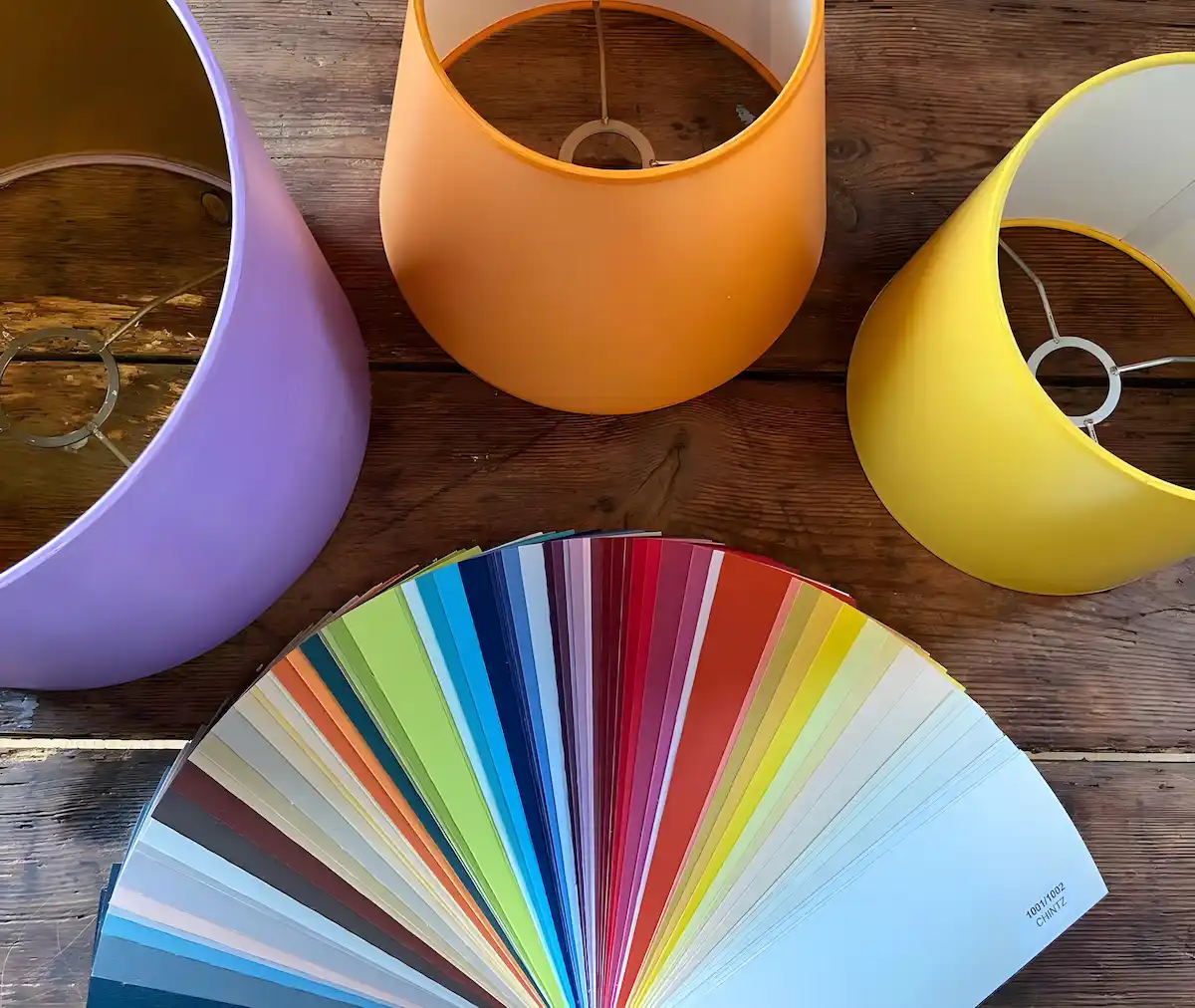 Drei bunte Lampenschirme und eine aufgefächerte Farbpalette auf einem Holztisch