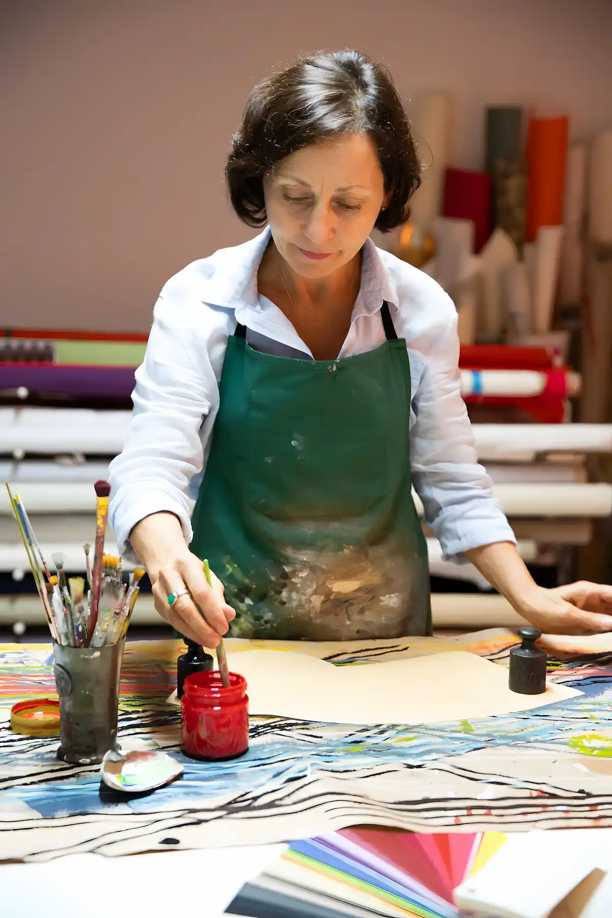 Marina Hummel mit grüner Schürze malt an einem Arbeitstisch mit Pinseln und Farbtöpfen