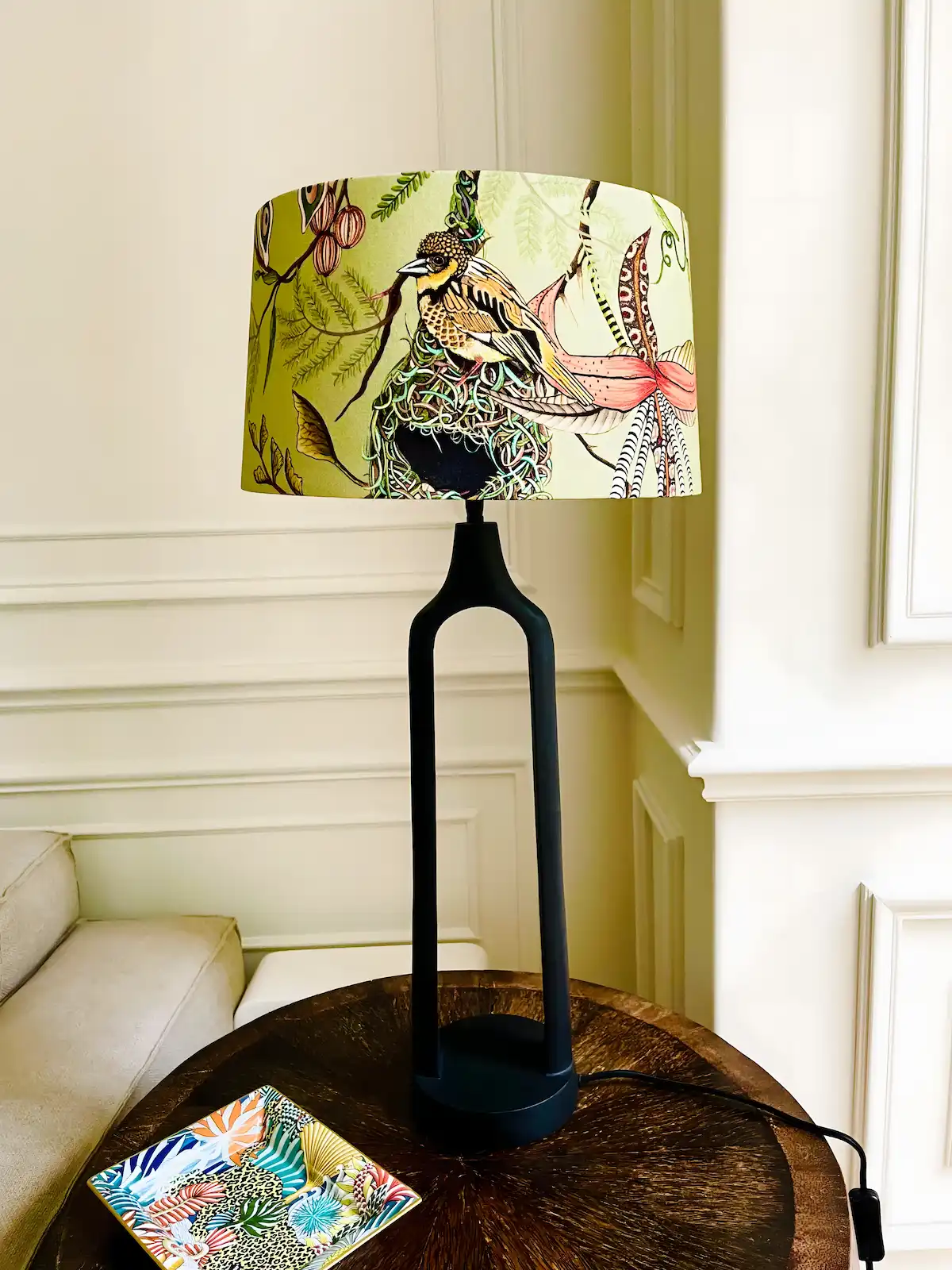 Runde Lampe mit Vogelmotiv auf dem Lampenschirm und schwarzem Ständer